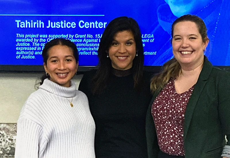 3 women standing side by side smiling in front of a screen with Tahirih information on it.