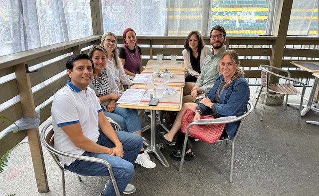 Mixed group of 7 adults sitting around a restaurant table smiling.