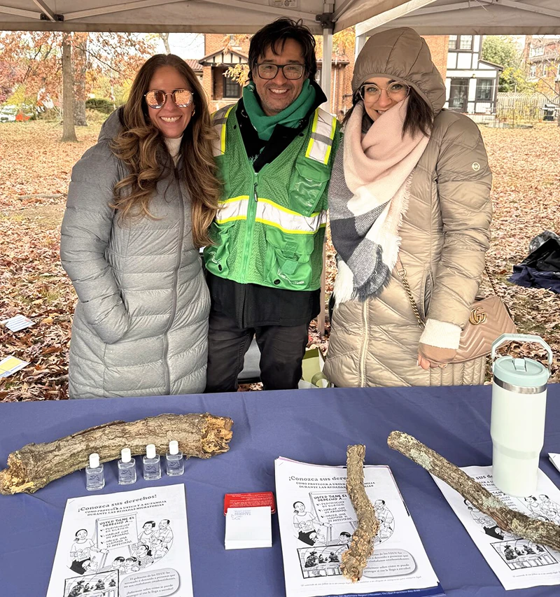 Three smiling adults in warm winter coats outside at a tabling event.