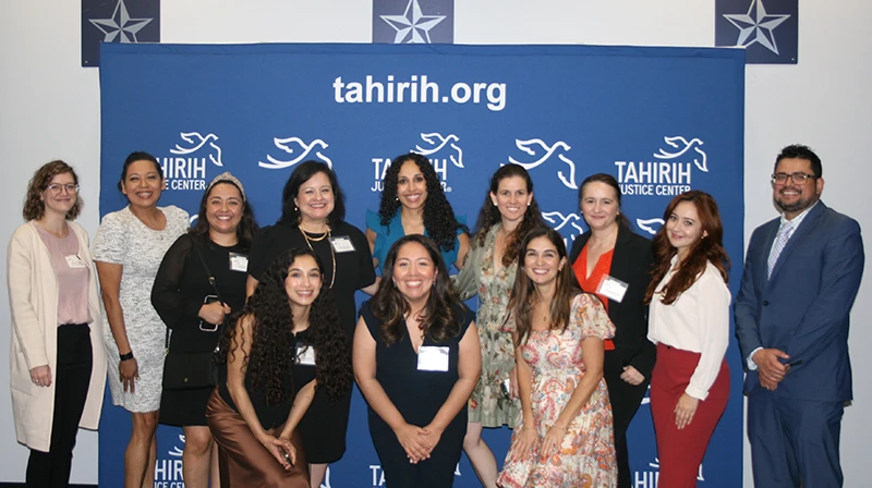 Mixed group of smiling people in front of a tahirih.org banner