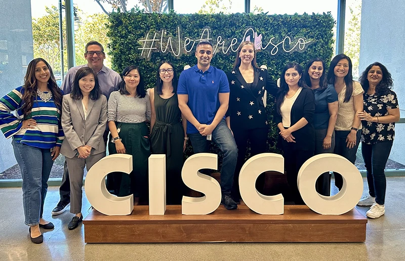 Group of professionals smiling and lined up behind a CISCO sign.