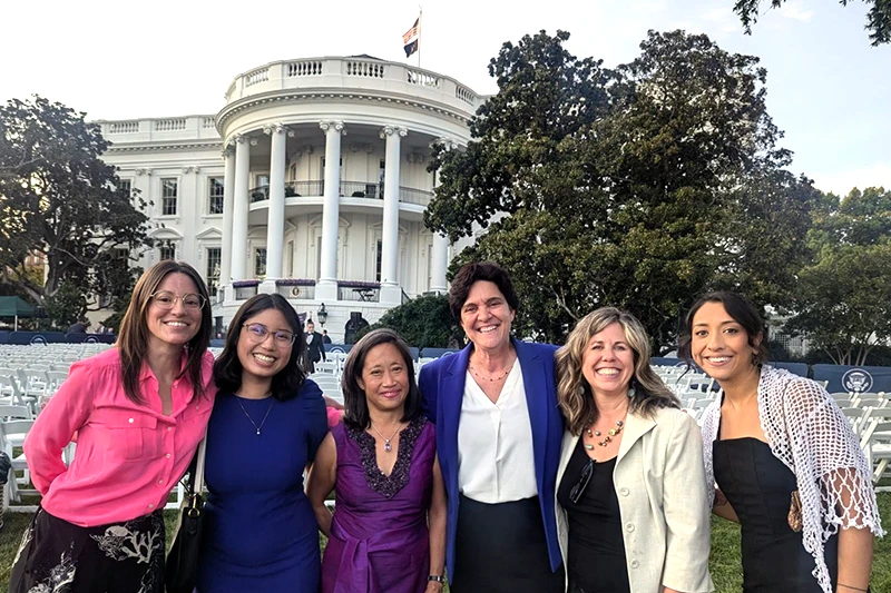 Six women arm in arm smiling in front of the White House.